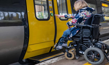A passenger using a wheelchair is waiting to board a 777 train. They have pressed the button to open the doors.  