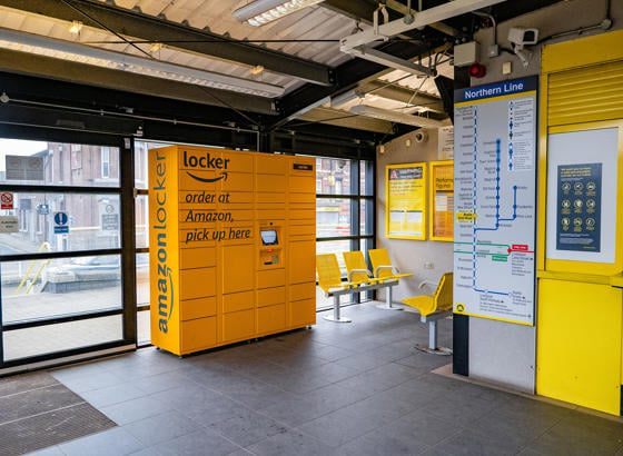 Amazon lockers at a train station seating area. There are information posters shown nearby. 