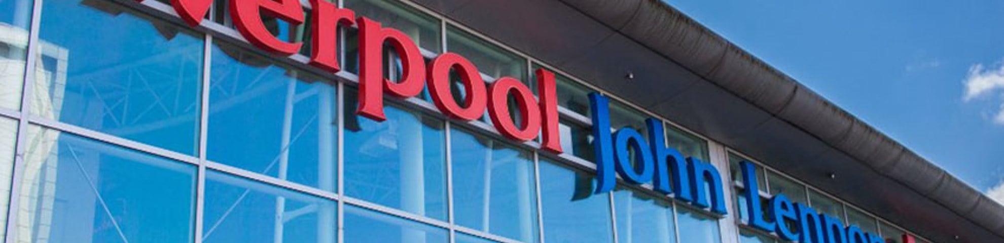 Signage of Liverpool John Lennon Airport's logo on a glass building. A blue sky appears above. 